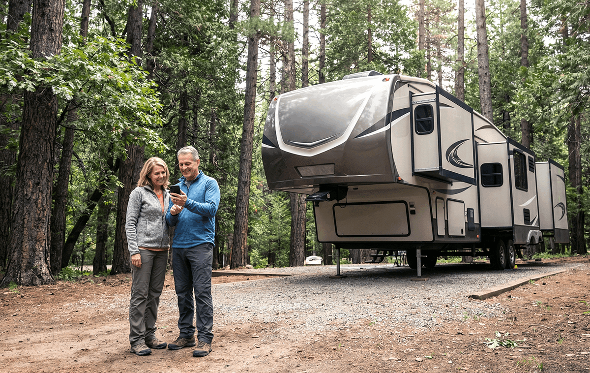 Couple standing in front of a 5th wheel RV pointing to their phone.
